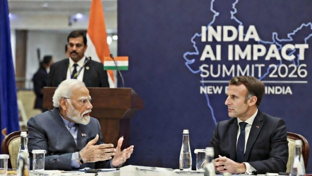 भारत एआई इम्पैक्ट समिट 2026 में प्रधानमंत्री नरेंद्र मोदी और फ्रांस के राष्ट्रपति इमैनुएल मैक्रों बैठक के दौरान चर्चा करते हुए, भारत मंडपम, नई दिल्ली में भारतीय और फ्रांसीसी झंडे पृष्ठभूमि में।
